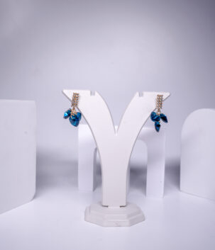Gold plated drop earrings featuring a crystal bar and cluster of blue heart-shaped crystals, displayed on a jewellery stand.