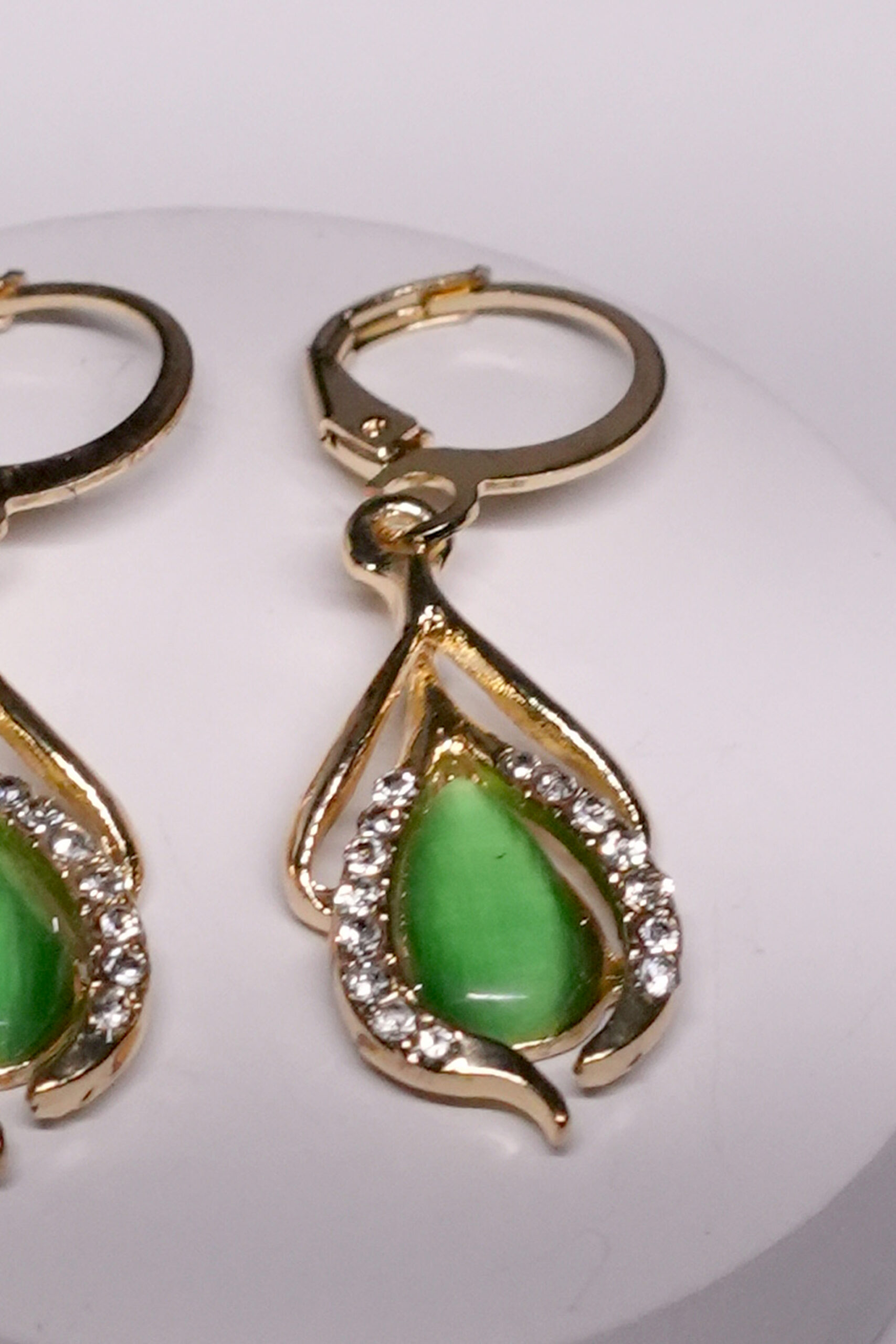 Close-up view of gold plated green stone drop earrings showing CZ stone detailing and lever-back closure.
