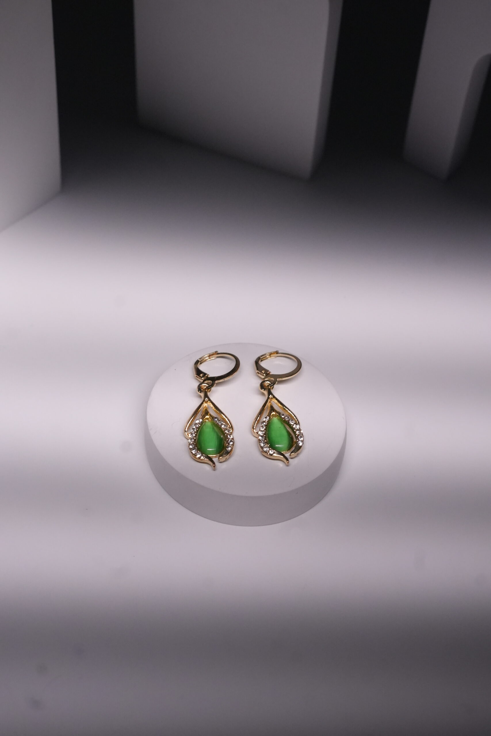 Gold plated drop earrings with green jade-toned stones and sparkling CZ detailing, displayed on a white jewellery stand.