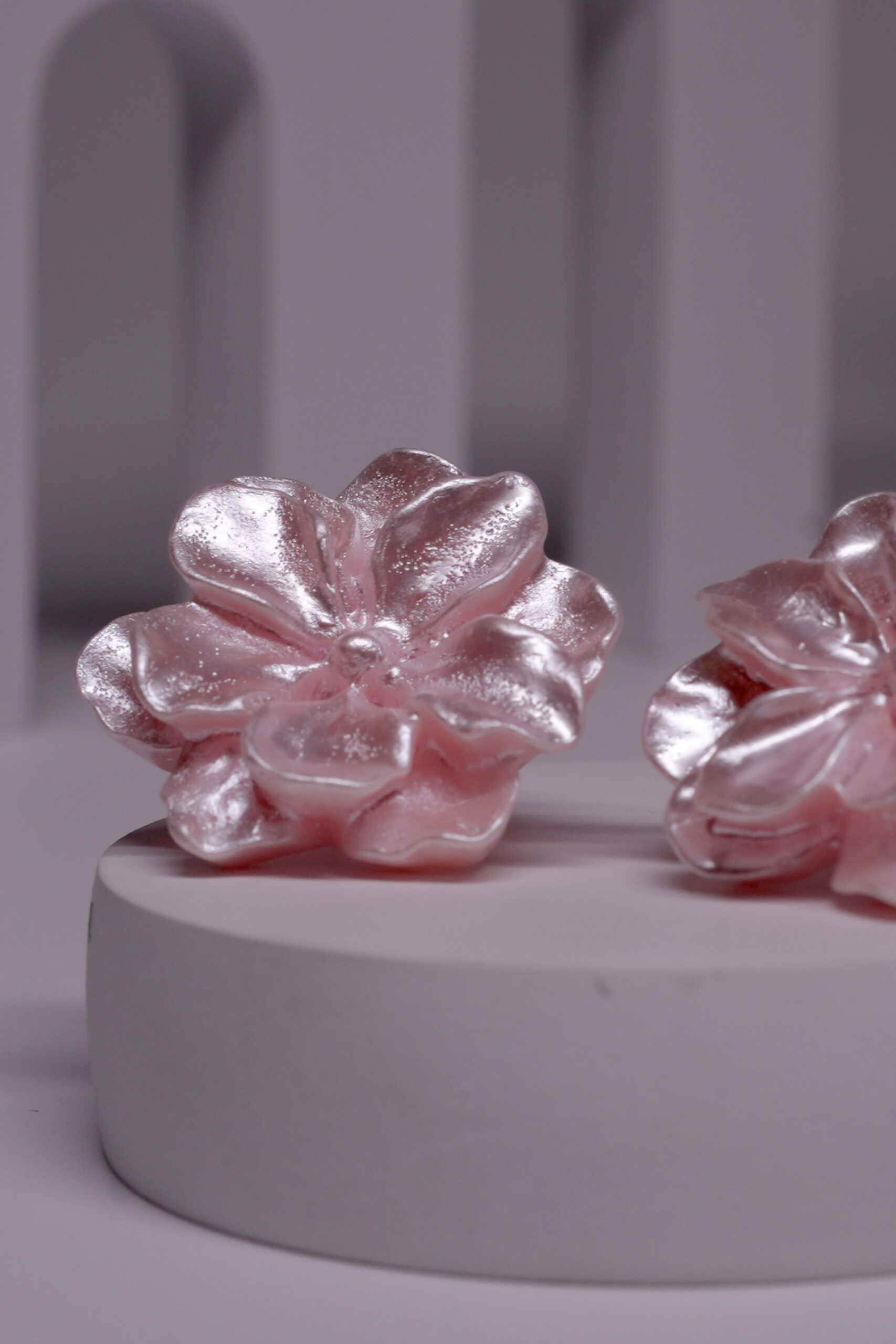 Close-up view of pink floral stud earrings showing textured petal detailing and metallic sheen.