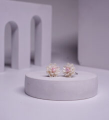Silver toned daisy-shaped stud earrings with a pink stone centre, displayed on a white pedestal.