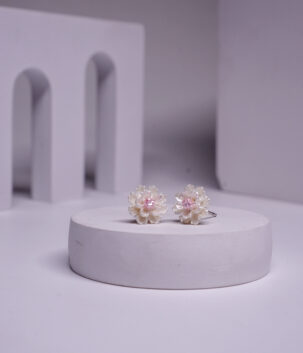 Silver toned daisy-shaped stud earrings with a pink stone centre, displayed on a white pedestal.