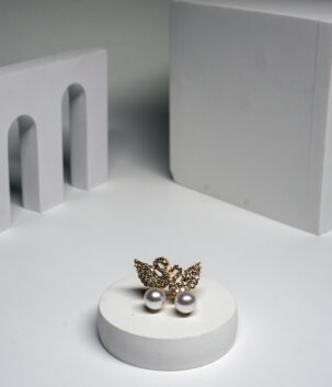 Gold plated swan stud earrings with crystal detailing and a pearl drop, displayed on a white pedestal.
