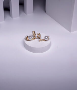 Gold plated curved stud earrings with a leaf motif and pearl accents, displayed on a white pedestal.