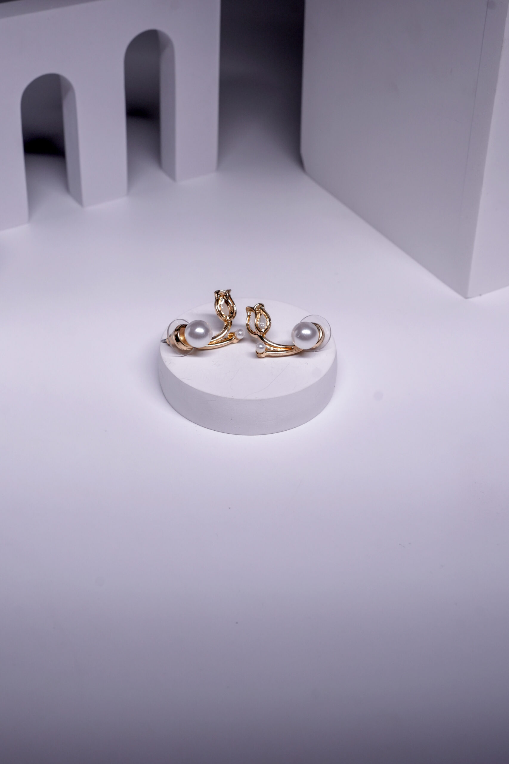 Gold plated curved stud earrings with a leaf motif and pearl accents, displayed on a white pedestal.