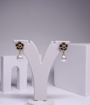 Gold plated black floral crystal earrings with a pearl drop, displayed on a jewellery stand.