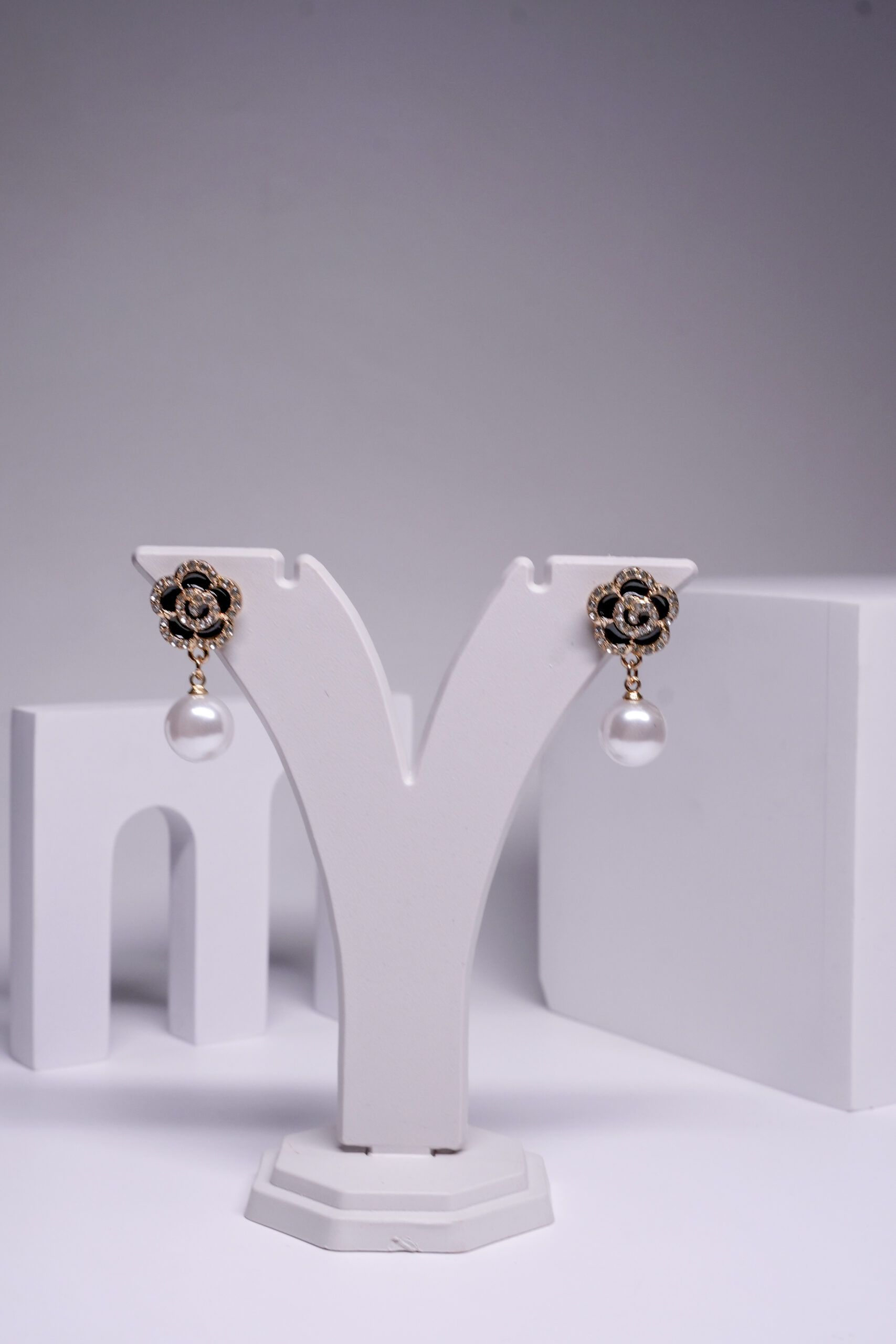 Gold plated black floral crystal earrings with a pearl drop, displayed on a jewellery stand.