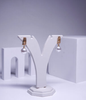 Gold plated crystal drop earrings with a hanging pearl, displayed on a jewellery stand.
