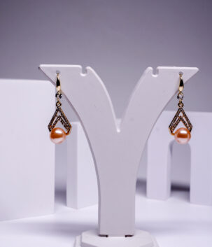 Gold plated dangle earrings with a pave crystal kite design and a peach pearl drop, displayed on a white jewellery stand.