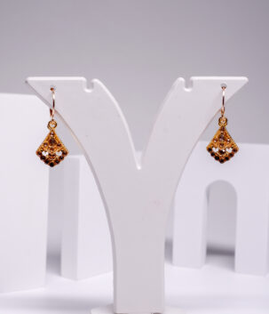 Gold plated fan-shaped drop earrings encrusted with topaz-toned crystals, displayed on a white jewellery stand.
