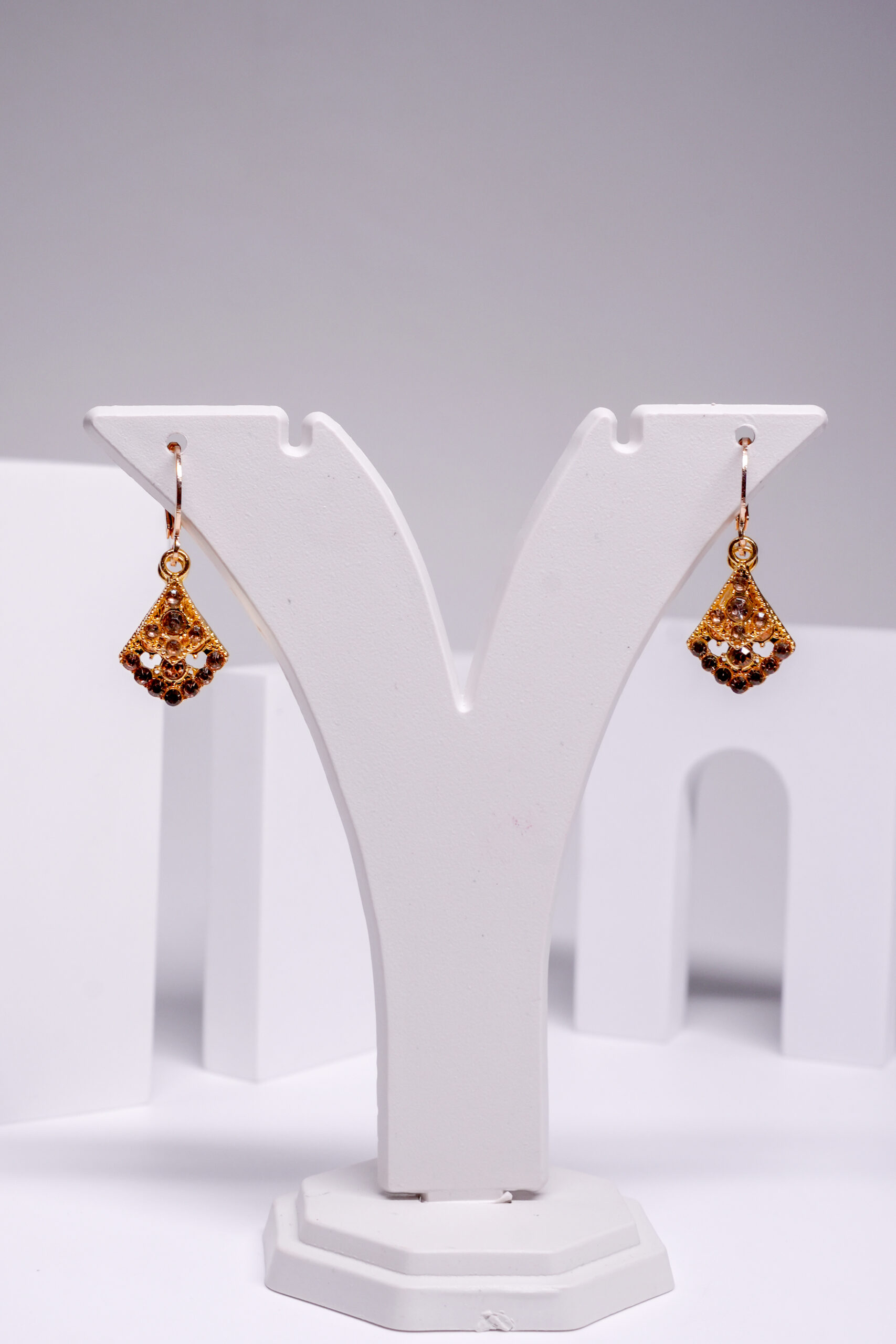 Gold plated fan-shaped drop earrings encrusted with topaz-toned crystals, displayed on a white jewellery stand.