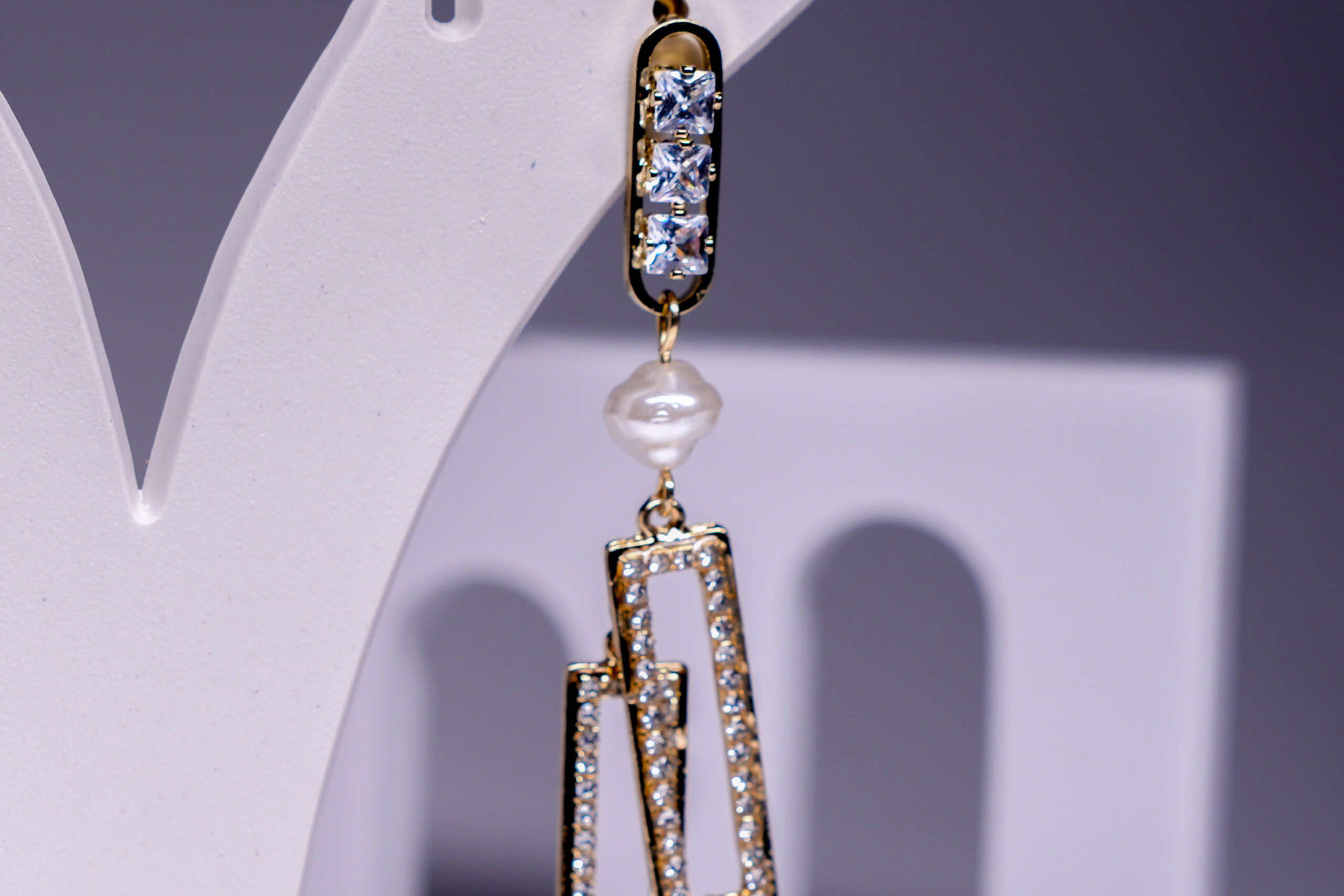 Close-up of gold plated crystal pearl earrings showing interlocking rectangular design and black enamel detailing.