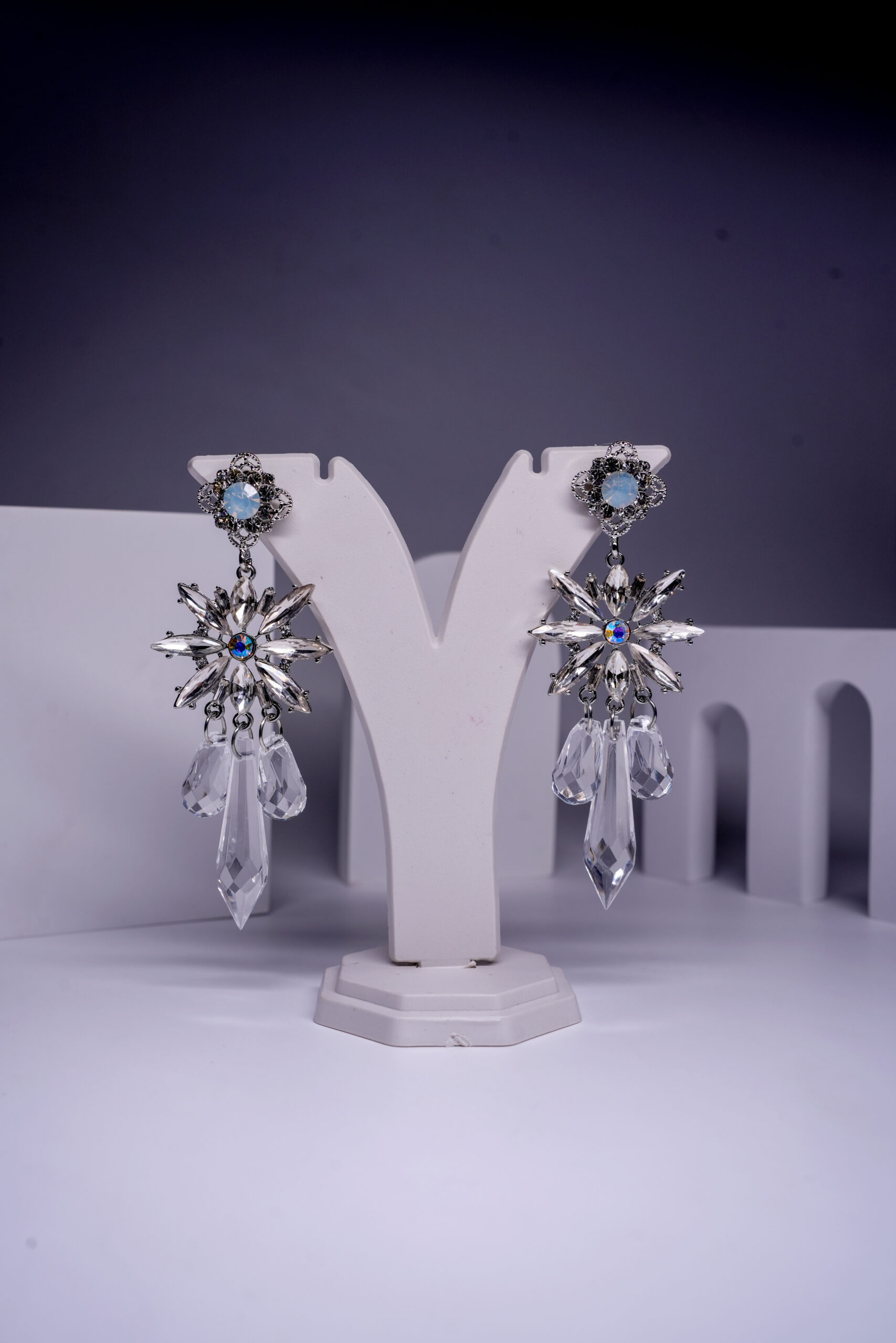 Silver plated opal crystal star drop earrings with faceted crystal drops, displayed on a white jewellery stand.