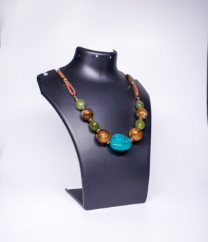 A handcrafted statement necklace with a large turquoise centrepiece, chunky tiger's eye and green jade beads, gold-tone accents, and a brown suede cord, displayed on a black jewellery bust.