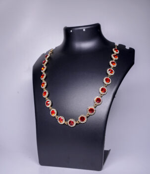Gold plated necklace with floral clusters of red crystals and sparkling stones, displayed on a black jewellery bust.