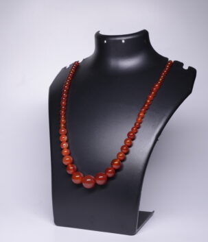 Graduated natural carnelian beaded necklace in warm reddish-orange tones, displayed on a black jewellery bust.