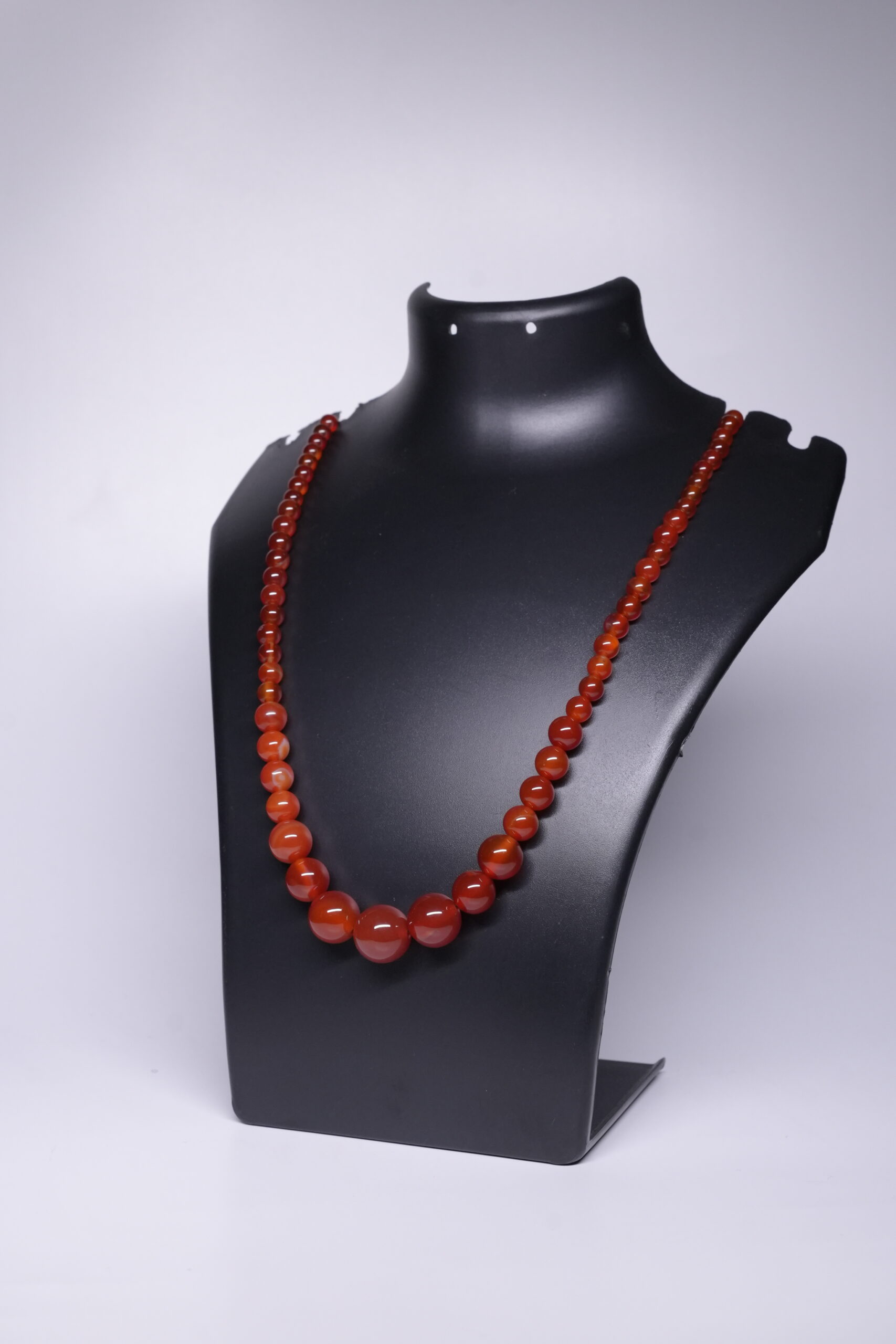 Graduated natural carnelian beaded necklace in warm reddish-orange tones, displayed on a black jewellery bust.