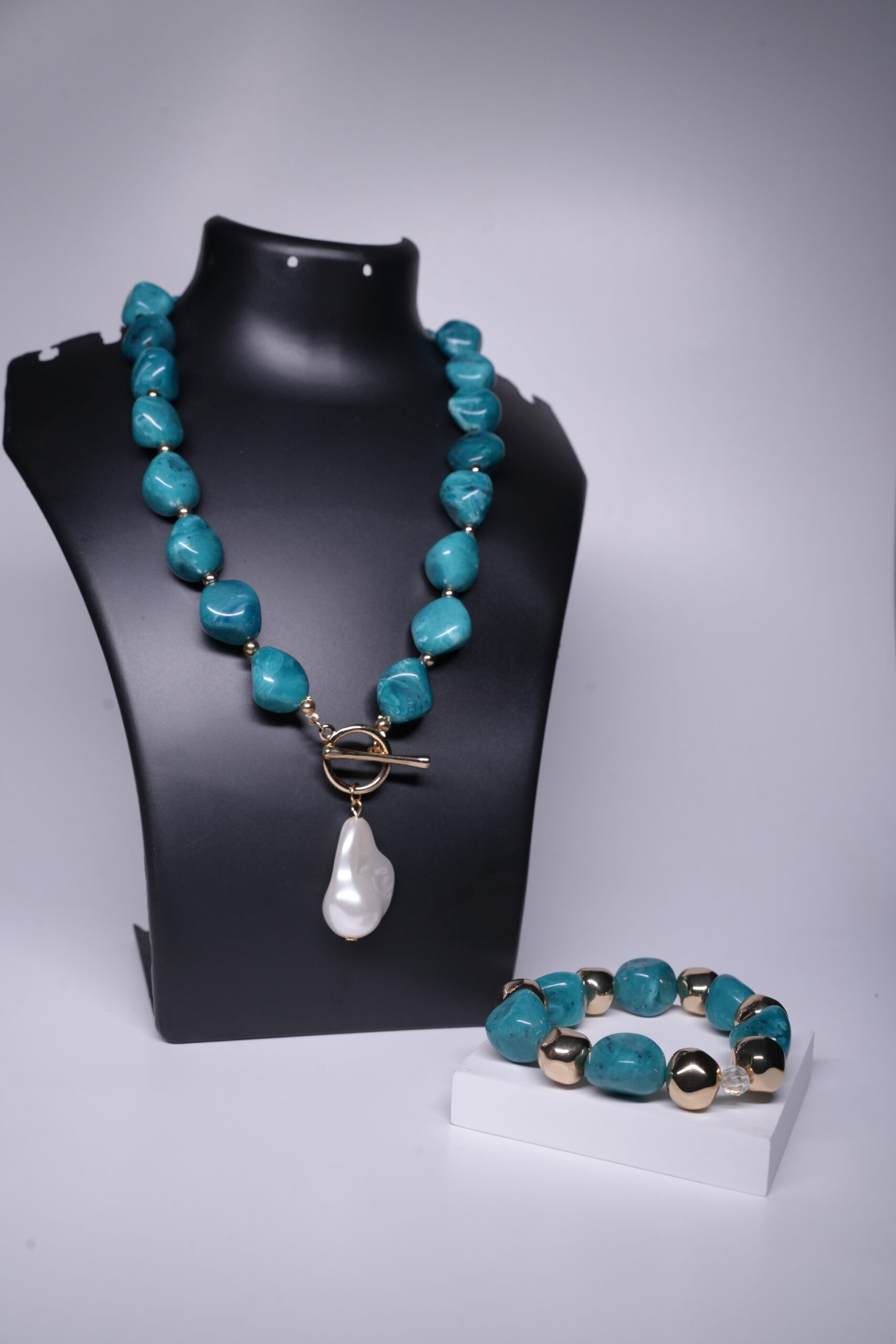 Turquoise nugget necklace with baroque pearl pendant and matching turquoise-gold bracelet displayed on a black jewellery bust and white stand.