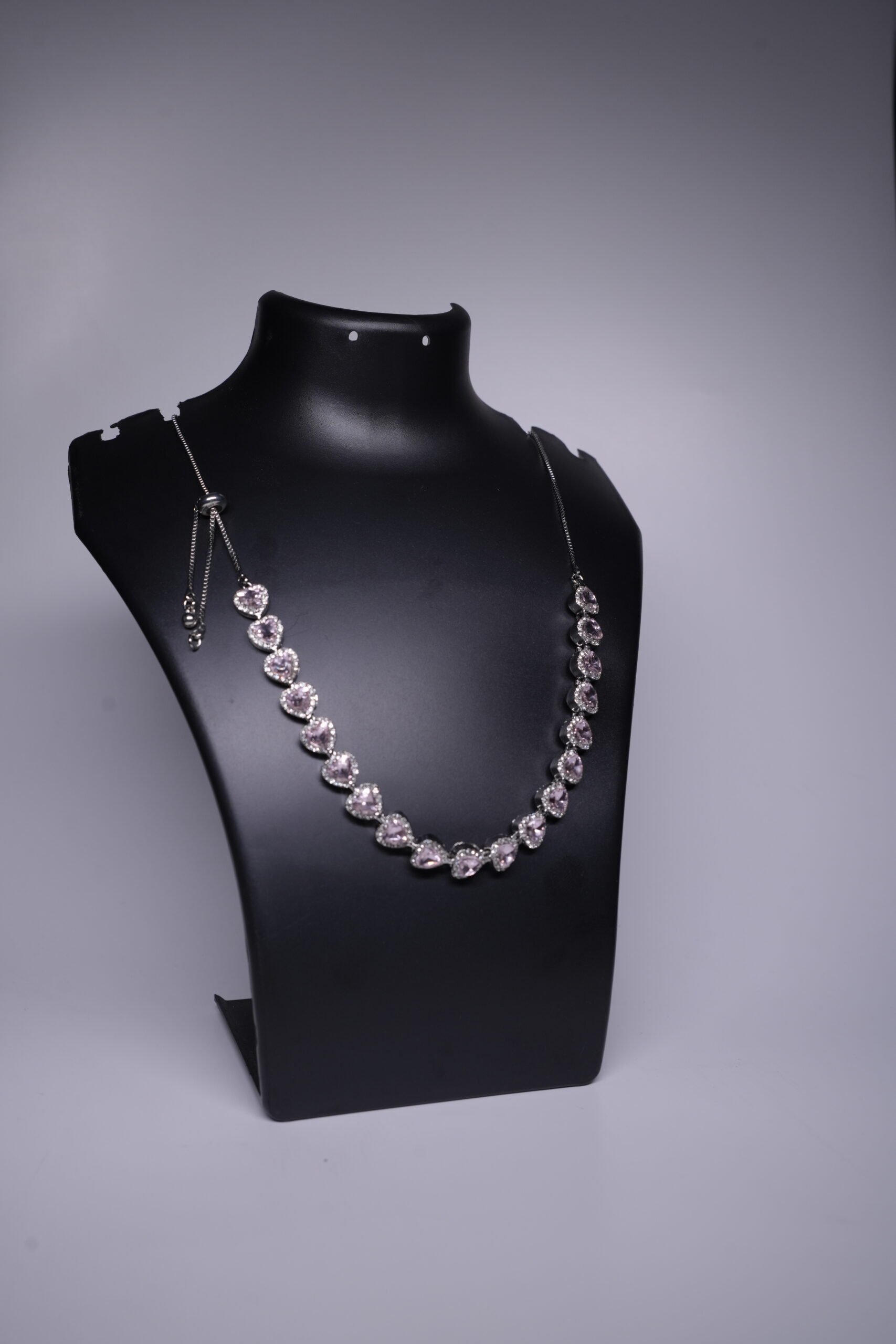 Silver rhodium plated necklace with heart-shaped pink stones and sparkling halo settings, displayed on a black jewellery bust.