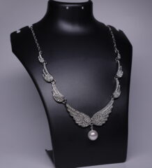 Silver rhodium plated necklace with crystal-studded angel wing motifs and a pearl drop pendant, displayed on a black jewellery bust.