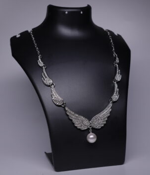 Silver rhodium plated necklace with crystal-studded angel wing motifs and a pearl drop pendant, displayed on a black jewellery bust.