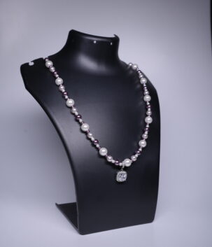 A silver toned necklace with white and plum pearls and a sparkling cushion-cut CZ pendant, displayed on a black jewellery bust.