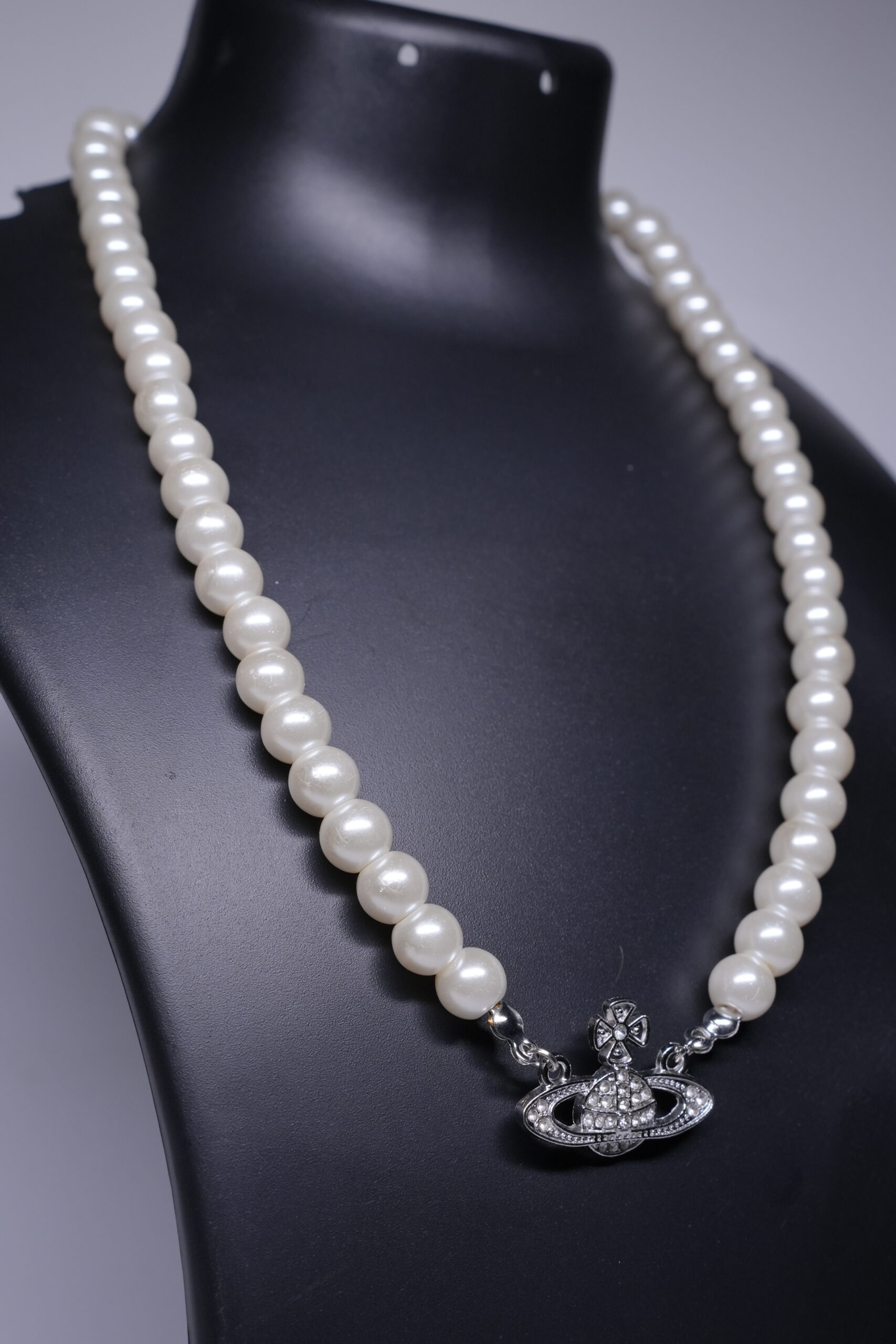 Close-up of pearl beaded necklace showing silver-toned orbit pendant with pave stone detailing.