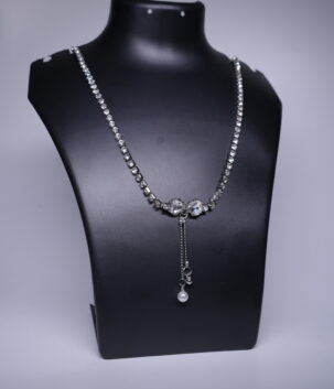 A silver toned CZ tennis necklace with a dainty pearl drop, displayed on a black jewellery bust.
