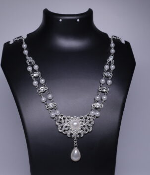 A silver toned bridal necklace with double pearl strands, sparkling CZ stones, and a filigree pendant with a pearl drop, displayed on a black jewellery bust.