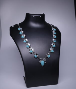 A silver toned boho necklace with turquoise stones, moonstone accents, and sparkling crystals, displayed on a black jewellery bust.