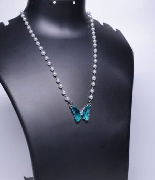 A silver plated faux pearl chain necklace with a sparkling teal crystal butterfly pendant, displayed on a black jewellery bust.
