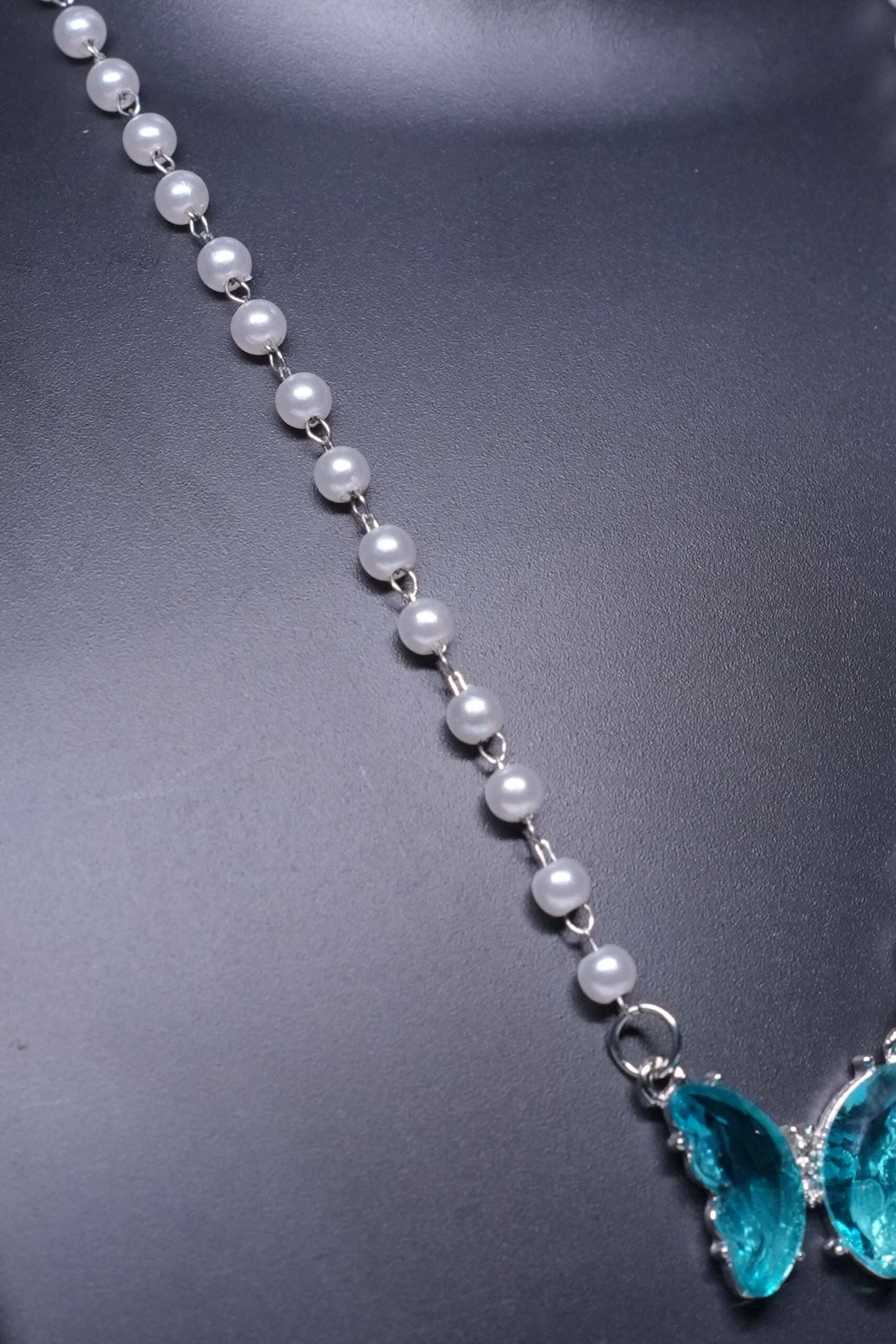 Close-up view of the pearl butterfly pendant necklace showing the teal crystal detailing and silver plated chain.