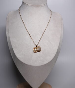 Gold plated heart pendant necklace from d2dazzle with a sparkling pavé zircon heart and an open heart holding a white pearl, on a fine gold sparkle chain displayed on a grey bust stand.